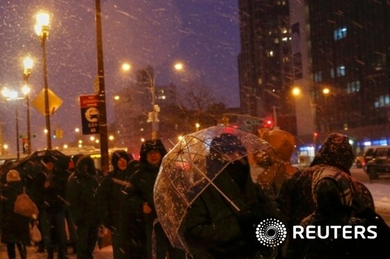People wait in line for public bus during snowfall in the Queens borough of New York