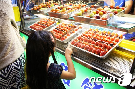 엄마와 함께 야시장을 찾은 한 소녀가 맛탕처럼 과일에 녹인 설탕을 바른 과일 꼬치(?)를 손가락을 가리키고 있다. 2015.11.17 뉴스1 트래블 © News1 travel 조용식 기자