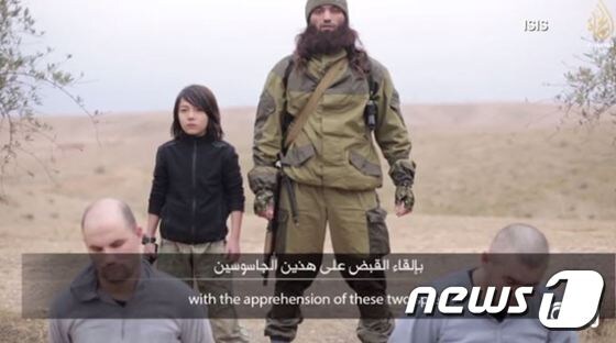 이슬람국가(IS)의 홍보 영상 속 한 소년이 권총을 들고 IS 대원과 함께 인질들 뒤에 서 있다. (CNN 캡쳐) <br />© News1