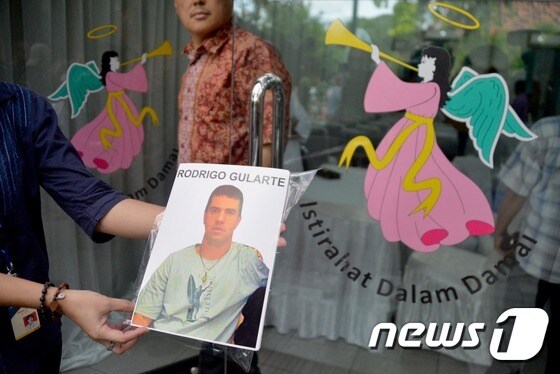 한 여성이 인도네시아에서 사형된 브라질 마약사범 로드리고 굴라르테의 사진을 들어보이고 있다. © AFP=뉴스1