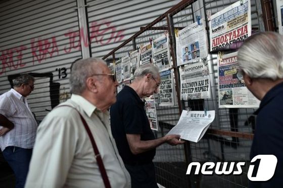 아테네 시민들이 그리스 소식을 전하는 신문을 유심히 들여다보고 있다 © AFP=News1