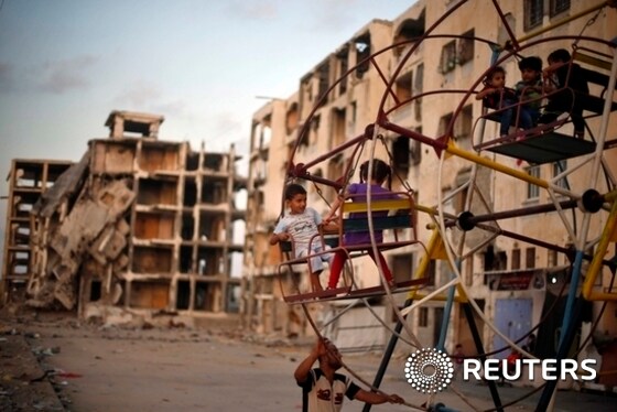 Palestinian children enjoy a ride on a ferris wheel near residential buildings, that witnesses said were destroyed by Israeli shelling during a 50-day war last summer, in Beit Lahiya town in the northern Gaza Strip