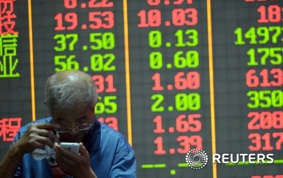 An investor checks on his mobile phone in front of an electronic board showing stock information at a brokerage house in Hangzhou