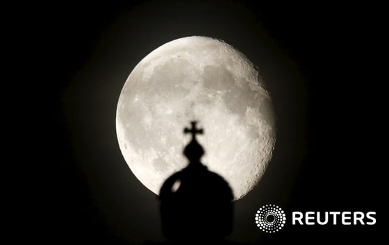 The moon rises next to a cross atop of the Reichstag building in Berlin