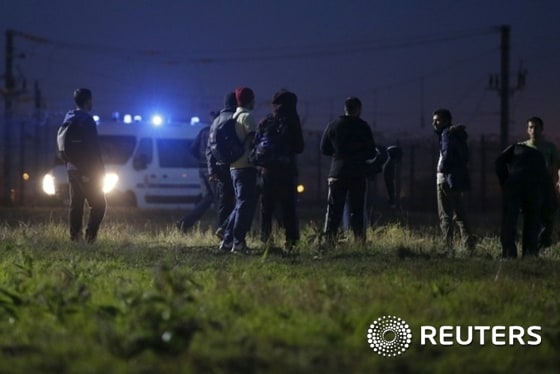 Migrants walk close to a Eurotunnel fence, as police arrive in a van, during an attempt to access the Channel Tunnel in Frethun, near Calais