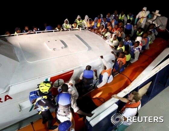 Rescued migrants climb onto an Italian Coast Guard vessel from the Migrant Offshore Aid Station ship MV Phoenix between Libya and the Italian island of Lampedusa