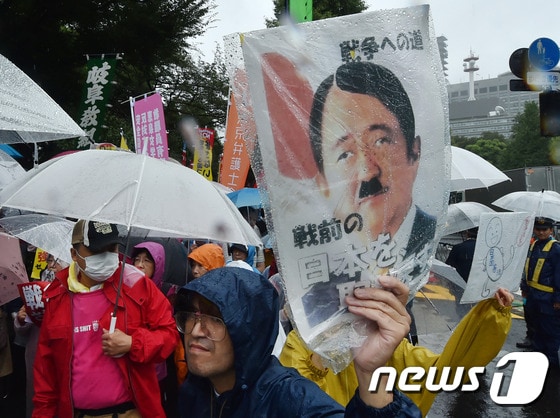 17일 안보법에 반대하는 일본 시민들이 국회의사당 앞에서 아베 신조 일본 총리를 아돌프 히틀러로 묘사한 포스터를 붙인 피켓을 들고 시위를 벌이고 있다. © AFP=뉴스1