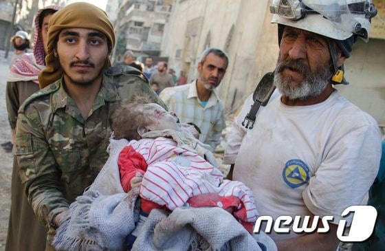 17일(현지시간) 시리아 알레포에서 '하얀 헬멧' 시리아 민방위대(SCD) 대원이 공습으로 무너진 건물 잔해에서 구조한 갓난아기를 안고 있다. © AFP=뉴스1