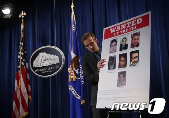 미국 법무부 관계자가 지난 24일(현지시간) 관련 발표에 앞서 금융회사와 댐 전산망 해킹 혐의를 받고 있는 이란인 7명의 사진을 설치하고 있다. © AFP=뉴스1