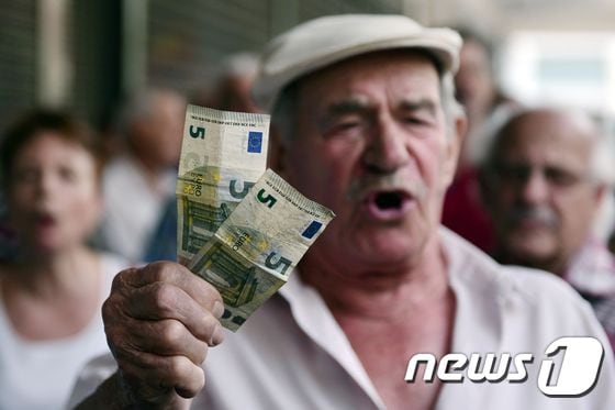 지난 2016년 그리스 아테네 노동부 청사 밖에서 시위를 하던 한 노인이 5유로짜리 지폐를 꺼내 흔들고 있다. <자료사진> / AFP PHOTO / LOUISA GOULIAMAKI