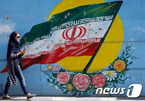 이란 국기 벽화 앞을 지나가는 이란 여성. © AFP=뉴스1