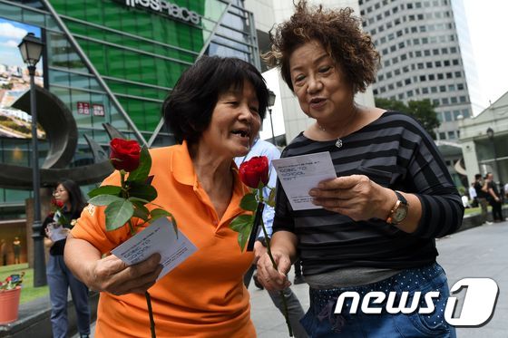 싱가포르 래플래 플레이스 앞. 광장 앞에서 열린 이벤트에서 받은 장미꽃과 카드를 읽고 있는 두 여성.© AFP=뉴스1