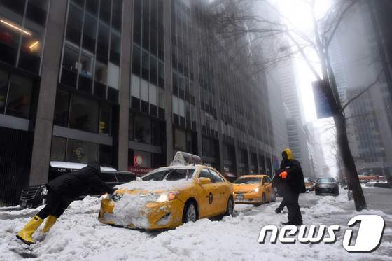 14일(현지시간) 미국 뉴욕 시내에서 한 남성이 눈에 파묻혀 멈춰버린 차를 밀고 있다. © AFP=뉴스1