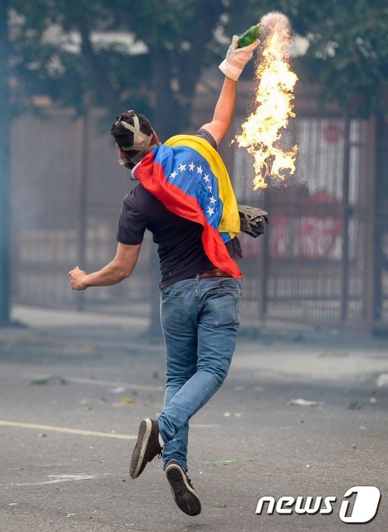 26일(현지시간) 베네수엘라 수도 카르카스에서 한 반정부 시위대가 경찰을 향해 병을 던지고 있다. © AFP=뉴스1