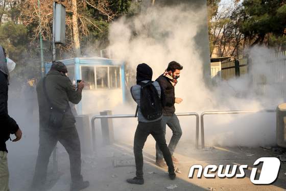 지난달 30일(현지시간) 이란 수도 테헤란에 있는 테헤란대학에서 시위가 벌어진 가운데 학생들이 최루탄 가스에 얼굴을 가린 채 도망가고 있다. © AFP=뉴스1