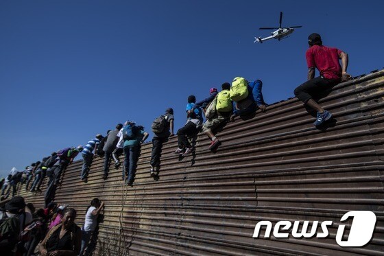 25일(현지시간) 멕시코 티후아나에 도착한 중미 이민자(캐러밴)들이 미국-멕시코 국경 펜스 위로 올라가고 있다. © AFP=뉴스1 © News1 우동명 기자