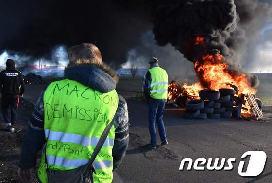  '마크롱 퇴진'이라는 글귀가 새겨진 노란조끼를 입은 남성이 11일(현지시간) 프랑스 남부 몽펠리에 인근 에마르그 불타는 타이어 앞에 서있다. © AFP=뉴스1