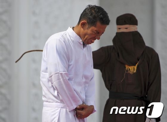 인도네시아 기독교인 조노 심볼론이 지난달 19일 아체주 반다 아체에 있는 이슬람 사원 앞에서 시민들이 보는 가운데 태형을 받고 있다. 그는 주류 판매로 샤리아법(이슬람율법)을 위반했다는 이유로 처벌을 받았다. © AFP=뉴스1