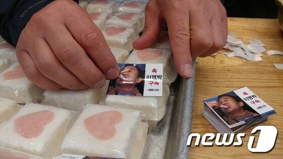 행사 주최 측이 떡 포장 표면에 '축 이명박 구속' 스티커를 붙이고 있다. (시민 제공)© News1