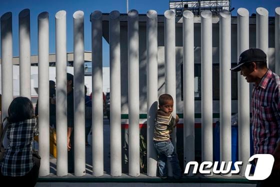 지난 9월12일(현지시간) 온두라스에서 온 한 어린 이민자가 미국-멕시코 국경에서 부모와 줄을 서서 기다리던 도중 벽에 매달려 장난을 치고 있다. © AFP=뉴스1