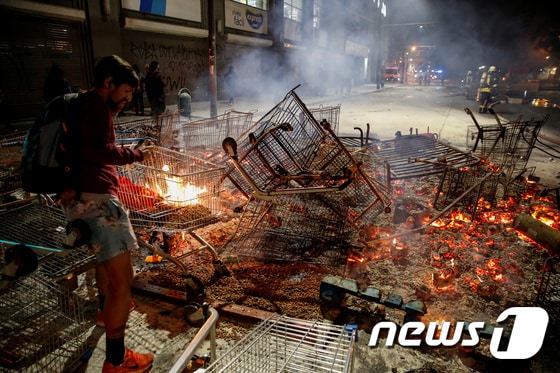 지난 19일(현지시간) 칠레 시위에 참가한 사람이 쇼핑카트 등에 불을 지르고 있다. @로이터=뉴스1