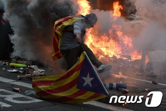 18일(현지시간) 스페인 바르셀로나 경찰 본부 근처에서 열린 카탈루냐 분리·독립 집회 도중 카탈루냐 깃발을 두른 시위자가 폭죽을 차고 있다. © AFP=뉴스1