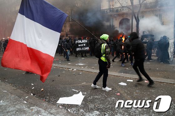 5일(현지시간) 프랑스 파리에서 열린 연금개편 저지 집회에서 프랑스 국기를 든 노란조끼 시위대가 최루탄을 들고 걸어가고 있다. © AFP=뉴스1