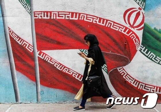 지난 7월22일(현지시간) 이란 여성이 테헤란의 거리를 따라 걷고 있다. 뒤로는 이란 국기가 그려진 벽화가 보인다. © AFP=뉴스1