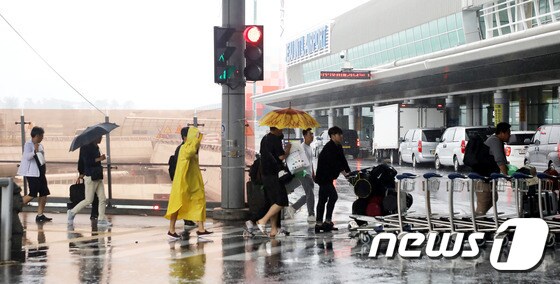 비가 내리고 있는 제주국제공항에서 항공기 이용객들이 우산과 우비를 쓰고 횡단보도를 건너고 있다.© 뉴스1 홍수영 기자