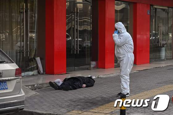 30일 중국 우한 시 한 가구점 앞에서 방호복을 입은 사람이 노인의 시신을 발견하고 어딘가로 전화를 하고 있다. © AFP=뉴스1