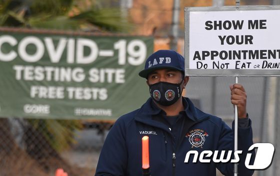 캘리포니아 소방 당국 관계자가 로스앤젤레스에 있는 신종 코로나바이러스 감염증(코로나19) 무료 진단검사소 앞에서 안내판을 들고 있다. © AFP=뉴스1
