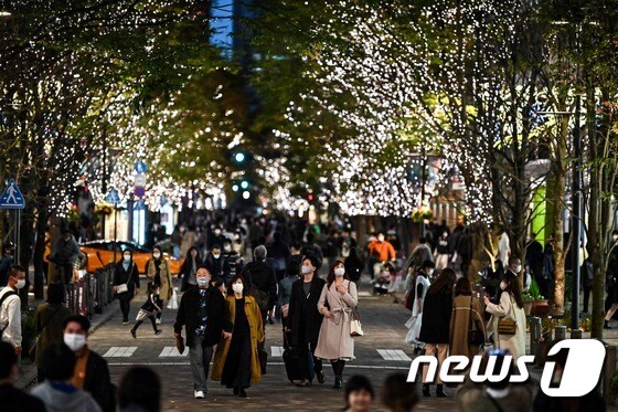 22일 도쿄의 한 거리에서 행인들이 전구로 장식된 가로수 아래를 지나가고 있다. © AFP=뉴스1
