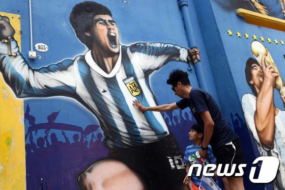 25일(현지시간) 부에노스아이레스 라보카 인근에서 아르헨티나의 축구 전설 디에고 마라도나를 묘사한 벽화 옆에서 한 남자와 아이가 헌화를 하고 있다. © AFP=뉴스1 © News1 이동원 기자