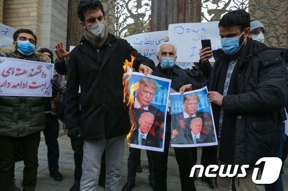 자국 과학자를 암살한 테러를 규탄하며 28일 시위를 벌이는 이란인들이 도널드 트럼프 미국 대통령과 조 바이든 대통령 당선인의 사진을 불태우고 있다. © AFP=뉴스1