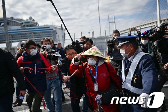 19일 일본 요코하마항에 정박 중인 크루즈선 다이아몬드 프린세스호에서 하선한 여성 승객이 취재진의 질문을 받으며 이동하고 있다. © AFP=뉴스1