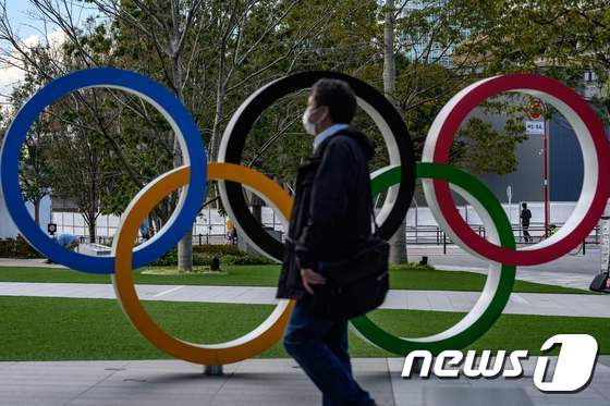 지난 11일 일본 도쿄에서 마스크를 쓴 한 남성이 올림픽의 오륜을 상징하는 조형물 앞을 지나가고 있다. © AFP=뉴스1