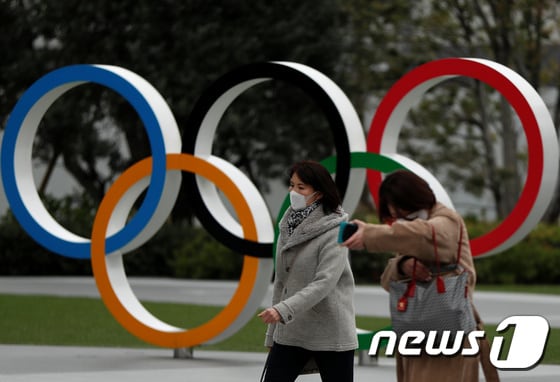 30일 일본 도쿄의 올림픽박물관 앞의 오륜 조형물 앞으로 마스크를 쓴 행인들이 지나가고 있다. © 로이터=뉴스1 © News1 송원영 기자