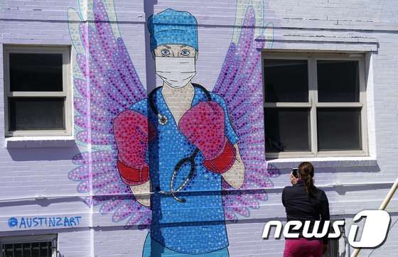 14일(현지시간) 미국 덴버 시내에서 한 여성이 복싱 장갑과 천사 날개, 마스크를 착용한 의료인을 묘사한 벽화 앞에서 스마트폰을 이용해 촬영을 하고 있다. © AFP=뉴스1 © News1 이동원 기자