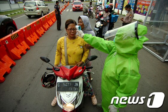 방역복을 입은 인도네시아 의료요원들이 태갈시내에서 통행인들이 열을 재고 있다. © 로이터=뉴스1