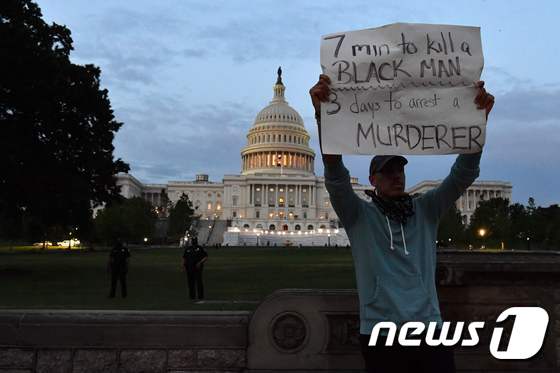 한 남성이 29일 미 국회의사당 앞에서 '한 흑인 남성을 살해하는 데는 7분, 살인자를 체포하는데는 3일이 걸렸다'고 쓴 미 정부를 비판하는 손팻말을 들고 있다. © AFP=뉴스1