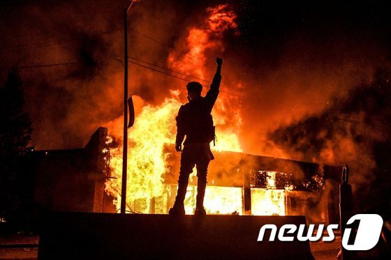 미국 미네소타주 미니애폴리스에서 29일 밤 벌어진 시위 중 한 남성이 불타고 있는 건물 앞에 서 있다. © AFP=뉴스1