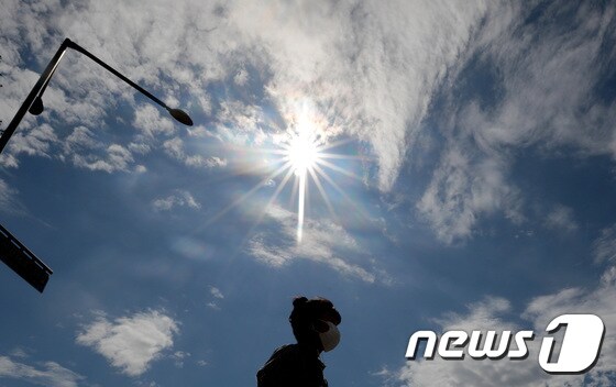 비가 그치고 맑은 날씨를 되찾은 지난 10일 오후 서울 중구에서 구름 사이로 드러난 태양 아래로 마스크를 착용한 한 시민이 지나가고 있다. 2020.7.10/뉴스1 © News1