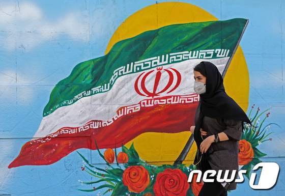 이란 국기 그림 앞을 한 여성이 지나가고 있다. © AFP=뉴스1