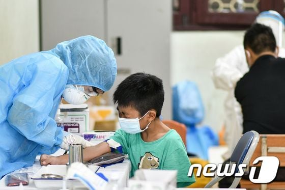 1일 베트남 하노이의 선별 진료소에서 보호복을 입은 의료진이 코로나19 검사를 위해 소년의 혈액 샘플을 채취하고 있다. © AFP=뉴스1