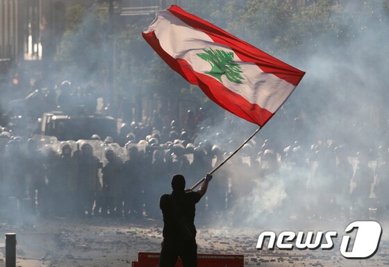 8일 한 시위대가 레바논 국기를 들고 반정부 시위를 벌이고 있다. 경찰은 최루탄으로 시위대를 진압하고 있다. © 로이터=뉴스1 © News1 박형기 기자