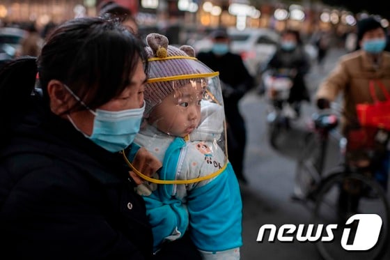 지난 13일 중국 후베이성 우한시의 쇼핑몰 앞에서 마스크를 쓴 한 여성이 아기를 안고 있다. © AFP=뉴스1
