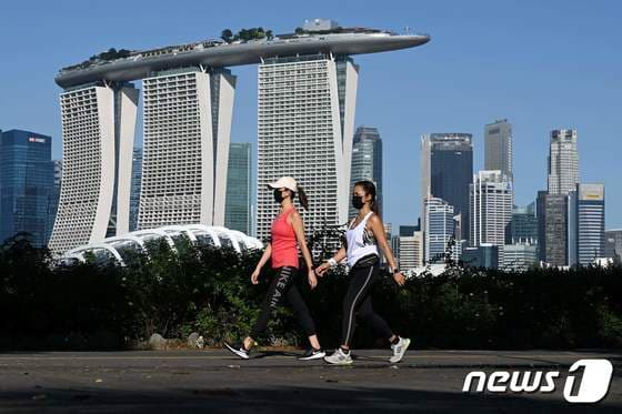 싱가포르의 랜드마크 마리나베이샌즈 호텔이 보이는 공원에서 2021년 8월 9일 산책하는 시민들의 모습. 싱가포르 재무··통상·보건 장관 3인으로 이뤄진 코로나19 태스크포스(T/F)는 지난 6월 말 스트레이트 타임스 기고문을 통해 최초로 '위드 코로나' 로드맵을 발표,해 세계의 이목을 끌었다. 다만 현재 싱가포르의 방역 수준은 한국보다는 훨씬 엄격하다. © AFP=뉴스1