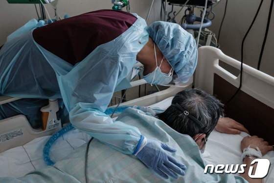 3일 (현지시간) 일본 삿포로에 있는 홋카이도 대학병원에서 방호복을 입은 의료진이 엎드려 있는 코로나19 환자를 위로하고 있다. © AFP=뉴스1 © News1 우동명 기자