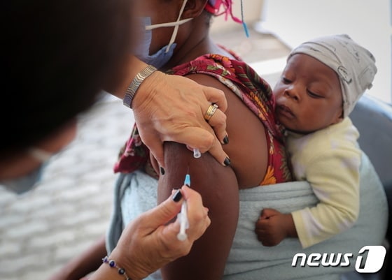 남아프리카공화국 요하네스버그 코로나19 접종소에서 2021년 12월 4일 한 여성이 아이를 업은 채 백신을 맞고 있다. © 로이터=뉴스1 © News1 최서윤 기자