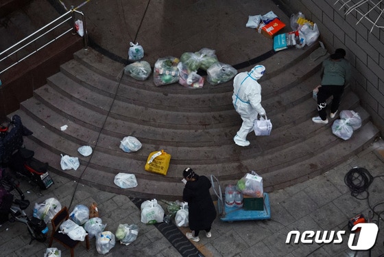24일 중국 수도 베이징에서 방역복을 입은 노동자가 봉쇄된 건물에서 배달 물품을 옮기고 있다. 2022,11.24 © 로이터=뉴스1 © News1 김정률 기자